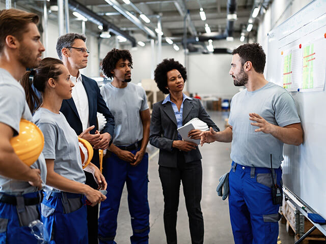 group of people standing in a factory holding hard hats