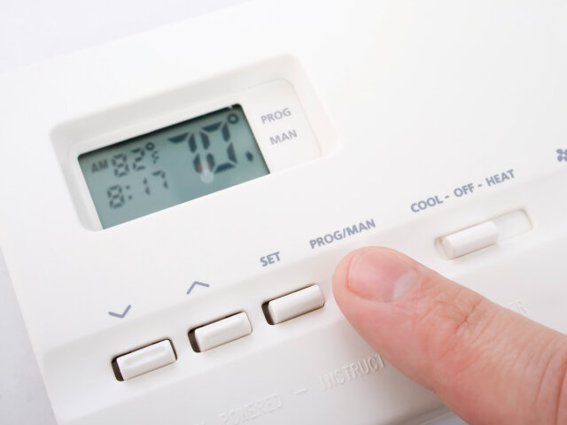 Finger point at a CTS tactile button on a digital thermostat