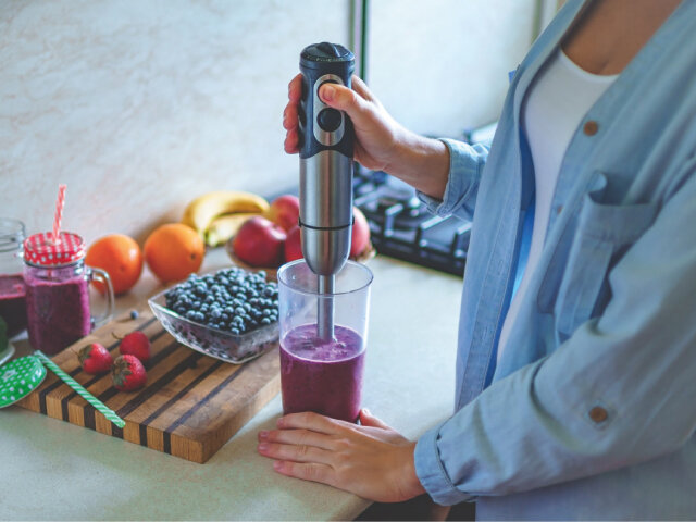 Women preparing a smoothie using a handheld mixer