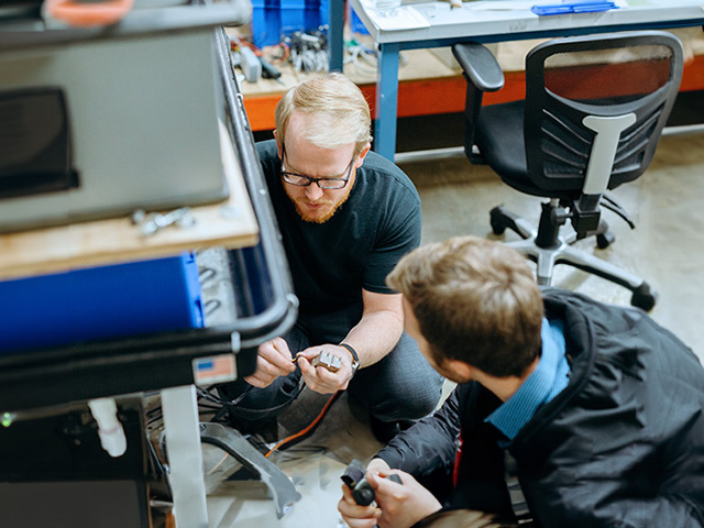 Two men kneeling and working on machinery