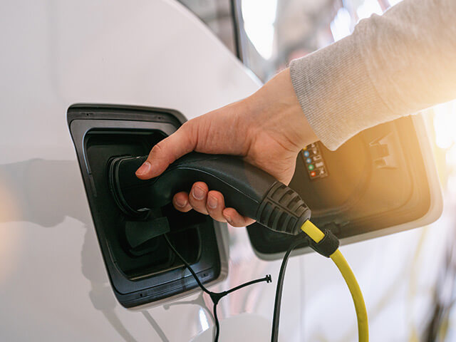 Person's hand plugging a charger into an electric car port with a sun glare