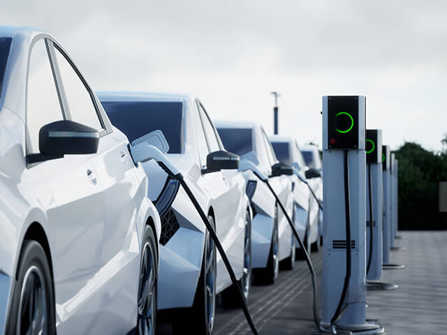 Electric cars lined up on curb, each connected to charging station