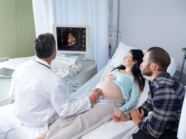 Ultrasound technician, man and woman looking at screen of 3D fetus