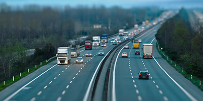 Cars traveling on six lane highway with blue and purple colored sky, green grass, and trees