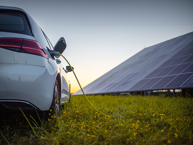 Electric car with charger plugged in and solar panels off in the distance